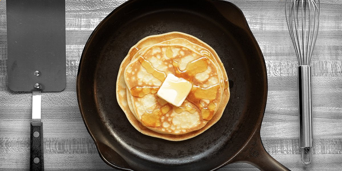 A cast iron pan full of pancakes with butter and syrup on top